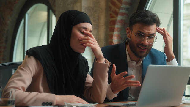 Multiethnic business colleagues Arabian Indian man Muslim woman in hijab looking laptop expect wish hope businesswoman businessman upset displeased bad result problem loss failure bankruptcy at office