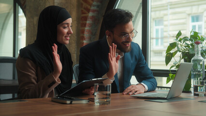 Arabian business colleagues two coworkers girl guy office employees male female muslim hijab woman man talk video call laptop online conference happy businessman businesswoman showing financial graph