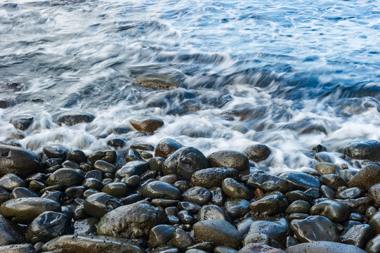 Shallow waves lapping against smooth wet cobblestones on a beach in Maui at sunset