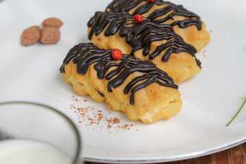 Chocolate Drizzled Eclairs with Red Garnish Side View on White Plate Indonesian Dessert Asian Food