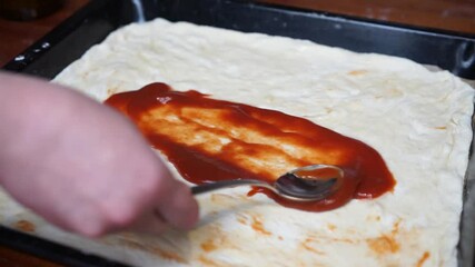 Making pizza at home, adding ketchup on a homemade pizza