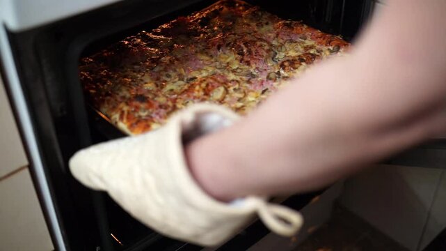 Woman's hands taking out homemade pizza from of oven
