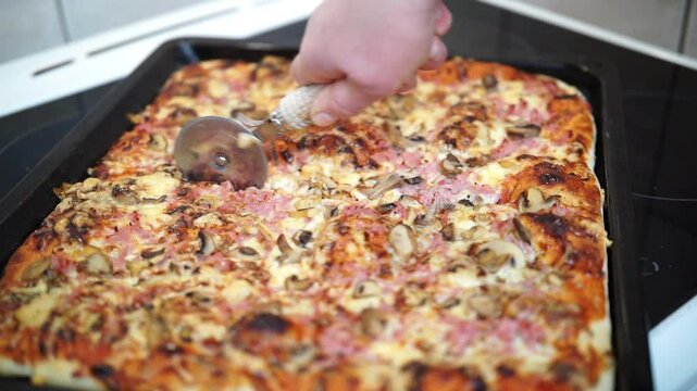 Woman's hand cutting pizza with pizza cutter wheel