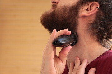 Man shaving with a cordless shaver. The man with a long beard. Cut a beard with electric razor shaver machine.