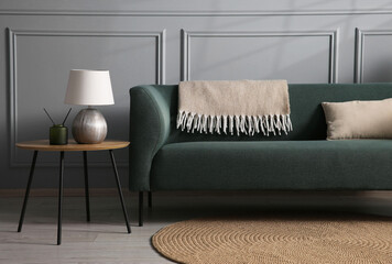 Comfortable sofa and side table near grey wall in room