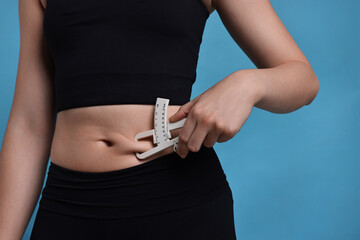 Woman measuring body fat with caliper on blue background, closeup