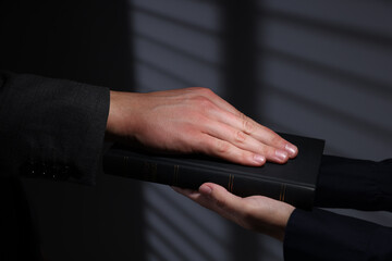 Man taking oath with his hand on Bible indoors, closeup