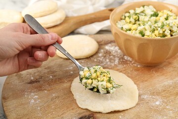 Woman making pirozhki (stuffed pastry pies) with eggs and dill at table, closeup