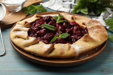 Tasty galette with cherries and mint on light blue wooden table, closeup