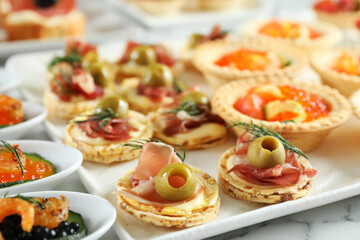 Many different tasty canapes on white marble table, closeup