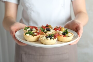 Woman holding plate with tasty canapes on light grey background, closeup