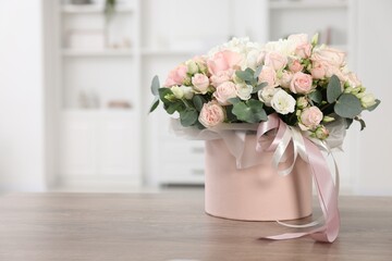 Gift box with bouquet of beautiful flowers and eucalyptus branches on wooden table against blurred background. Space for text