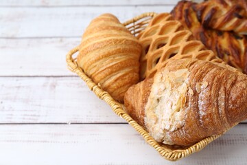 Different pastries in basket on white wooden table, closeup. Space for text