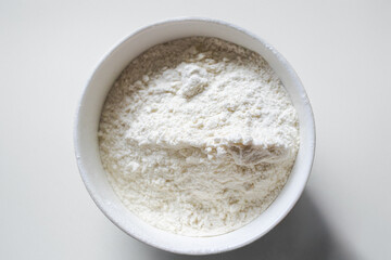 Close up of white flour, flour on a bowl on a white background, ingredient for food preparation. Isolated on a white background. Top view. White flour in a white bowl on a white background.