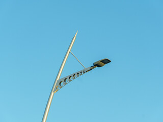 A modern streetlight is prominently displayed against a clear blue sky. The light features an artistic shape with circular cutouts, showcasing innovative urban design and functionality.