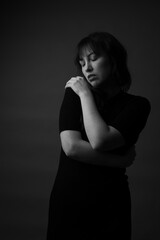 Obraz premium Black and white dark portrait of a caucasian woman hugging herself with her eyes closed. She is wearing a black dress. This is a moody portrait. 