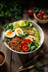 Buckwheat groats with avocado, various vegetables and soft-boiled egg in a ceramic bowl on a wooden table, close-up. Healthy breakfast suggestion slavic girl diet