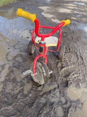Kids red balance tricycle stuck in springtime mud