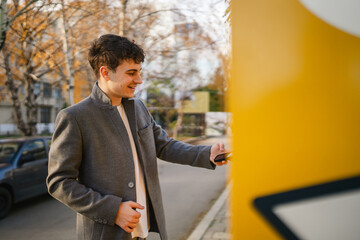 young man scan qr code with smart phone on parcel machine outdoor