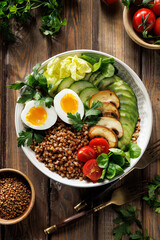 Buckwheat groats with avocado, various vegetables and soft-boiled egg in a ceramic bowl on a wooden table, top view. Healthy breakfast suggestion slavic girl diet