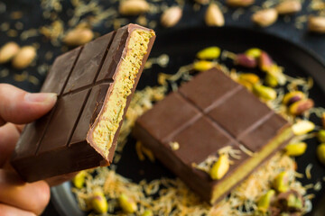 A hand holds sliced ​​Dubai Chocolate on a black plate