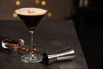 Glass with delicious espresso martini, coffee beans and jigger on table in bar. Space for text