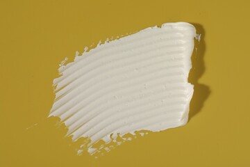 Cream on dark yellow background, top view. Sample of cosmetic product