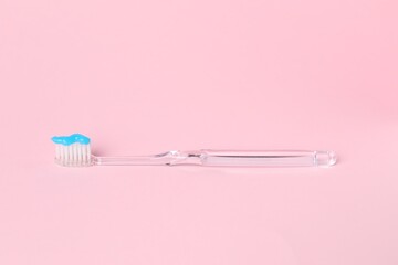 One toothbrush with toothpaste on pink background
