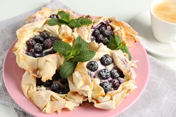 Tasty puff pastries with blueberries, powdered sugar, mint and coffee on table, closeup