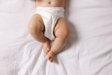 Cute little baby in diaper on bed, top view