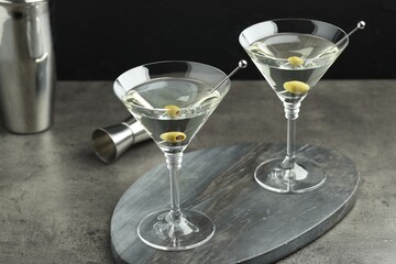Martini cocktail with olives in glasses on grey table against black background