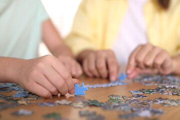 Fototapeta premium Mother and her daughter solving puzzle together at wooden table indoors, closeup
