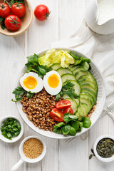 Buckwheat groats with avocado, various vegetables and soft-boiled egg in a ceramic bowl on a white table, top view. Healthy breakfast suggestion slavic girl diet