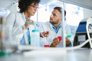 Fototapeta premium Two biotechnologists cooperating while analyzing antiviral drug in laboratory. Focus is on man.
