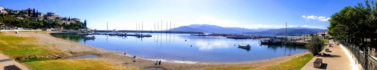 Panorama of Astros, a picturesque coastal town in Peloponnese, Greece, featuring its serene fishing shelter and clear azure waters. 