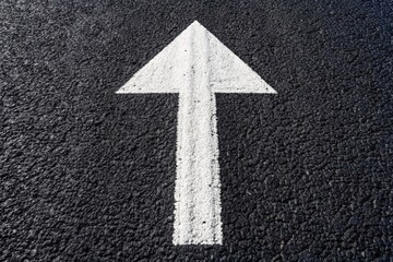An aerial shot captures a white arrow road sign on dark asphalt, representing direction and forward movement in city landscapes for enhanced navigation.