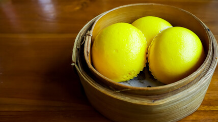 Three golden-yellow baozi chinese steamed buns arranged in a bamboo steamer basket, placed on a wooden table, exuding a warm and appetizing appearance