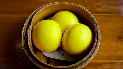 Three golden-yellow baozi chinese steamed buns arranged in a bamboo steamer basket, placed on a wooden table, exuding a warm and appetizing appearance