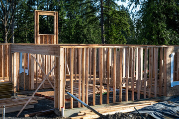 New house construction in progress, glue laminate beam supporting second floor, walls and window wood framing, evergreen trees in background

