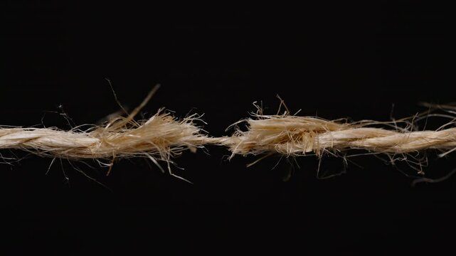 Close-up of a frayed rope on the verge of snapping, showing tension and stress in the fibers against a black background. jute or hemp rope
