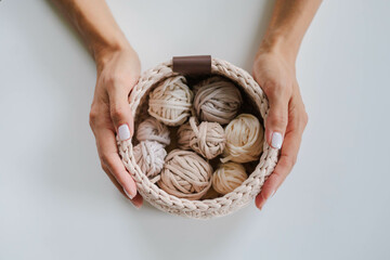 Female hands holding a crocheted basket with skeins of cotton yarn in natural tones and colors.