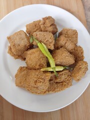 Indonesian Popular Street Food - Tahu Bandung (Fried Tofu) that contain lots of vegetable protein because they are made from soybeans on White plate with wooden background with green chili on it