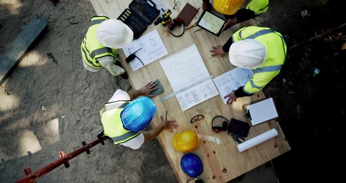 Architecture, collaboration and planning with construction worker team on building site from above. Engineering, infrastructure and meeting with industrial people at table for design discussion