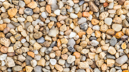 Naklejka premium Close-up view of a pile of small, multicolored pebbles. The stones are various shades of beige, tan, gray, and white, creating a textured and natural background.