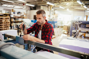 Male technician adjusting machinery in a busy printing press facility