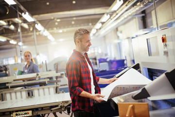 Focused male worker inspecting large printouts in industrial printing facility
