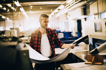 Focused male worker inspecting large printouts in industrial printing facility