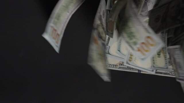 Hundred-dollar bills scatter and fly out of the frame, leaving a single bill on the black background, symbolizing financial depletion or the last remaining resource.
