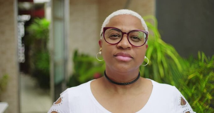 Close-up portrait of a woman with short white hair and glasses, confident and composed expression, showcasing individuality and personal style in outdoor setting