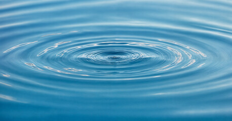 A single water droplet creates concentric ripples on a serene blue surface, capturing the elegance of motion and the tranquility of nature. This image symbolizes simplicity, purity, and the ripple eff